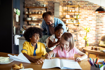 Multiracial children studying and playing with father in kitchen