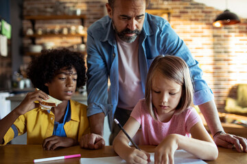 Father helping children with homework at kitchen table