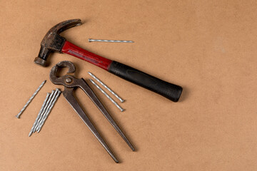A red carpenter's claw hammer and nail tongs with nails on a wood surface

