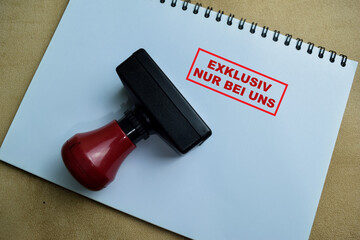 Red Handle Rubber Stamper and Exklusiv Nur Bei Uns text above book isolated on wooden background