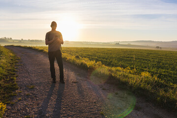 Man, traveler using mobile phone walking in morning spring fog Czech landscape at sunrise