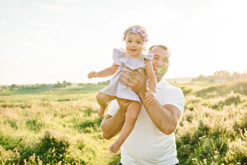 Kid funny with parent in grass field at sunset. Father holds throws up happy daughter plays in...