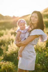 Fototapeta premium Young mother kissing baby girl walk in park. Family holiday in garden. Portrait mom with child together on nature. Mum, little daughter outdoors. Happy Mothers Day. Close up.