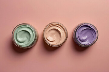 Three jars of green, beige and purple foundation on a pink background, top view, splashes of cream. Banner template for advertising cosmetics, concealer.