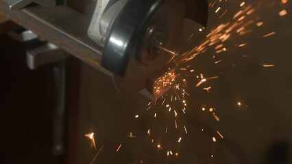 Craftsman in protective gloves working with grinder at industrial plant, man grinding iron detail, sparks flying around, view from glass sheet.