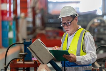 Asian male engineer in uniform inspection warehouse and check control heavy machine construction...