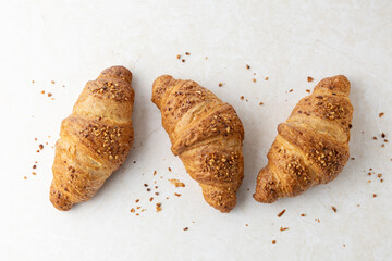 Fresh baked crushed nut croissants with crumbs on light marble table background.