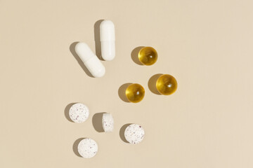 White and yellow capsule pills on beige isolated background with glass of water. Concept of pharmacy, daily intake of pills, vitamins to improve health and beauty.