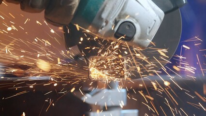 Craftsman working with grinder at industrial plant, man grinding iron detail, sparks flying around...