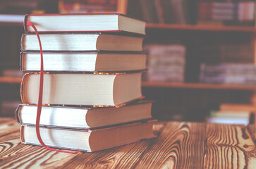 A stack of old books on table against background of bookshelf in library. Conceptual background on...