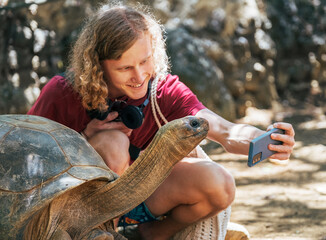 Smiling tourist boy making a selfie using cell phone with Aldabra giant tortoise endemic species -...