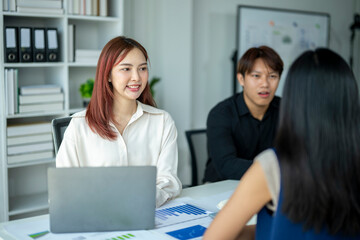 A woman is sitting at a desk with a laptop and a man and woman are talking to her