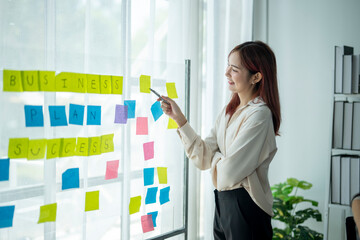 A woman is pointing at a board with colorful sticky notes on it. The board has the words 