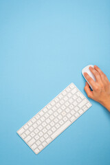 a person is using a computer keyboard with a mouse on a blue background. Copy space