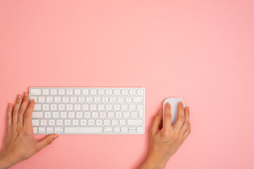 a person is using a computer keyboard with a mouse on a pink background. Copy space