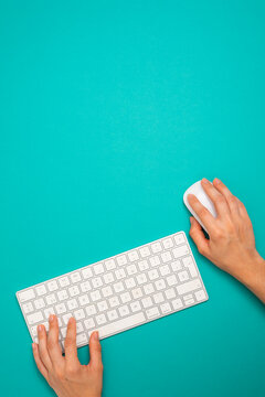 a person is using a computer keyboard with a mouse on a turquoise background. Copy space