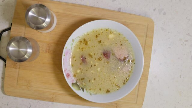 Top view of traditional Polish zurek soup or white borscht in a bowl. Tasty soup with sausages and eggs on wooden cutting board
