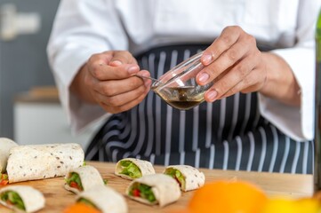 chef make tortilla wrap vegetable salad slice by knife on cutting board and mix sour salad dressing in small bowl glass with wine and olive oil. tortillas wrap vegetable and juicy liquid sour dressing