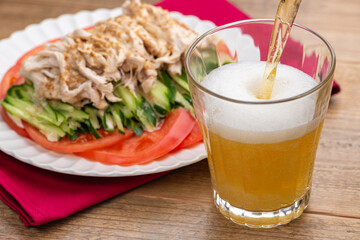 グラスに注がれるビールと棒棒鶏（バンバンジー）