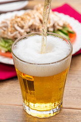 グラスに注がれるビールと棒棒鶏（バンバンジー）