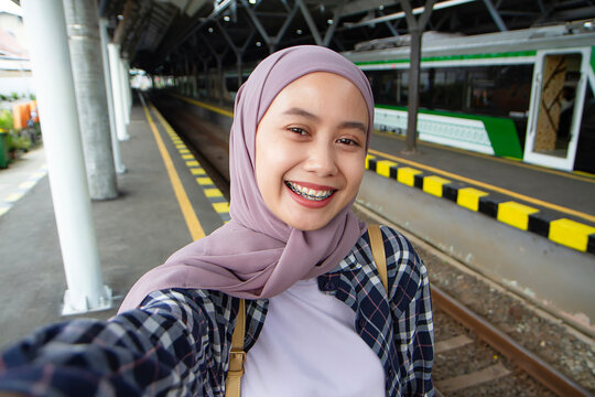 pov of selfie shoot happy asian muslim woman with smile on her face at train station. traveling concept