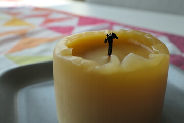 Half-burnt pillar candle made of beeswax on a colorful table runner