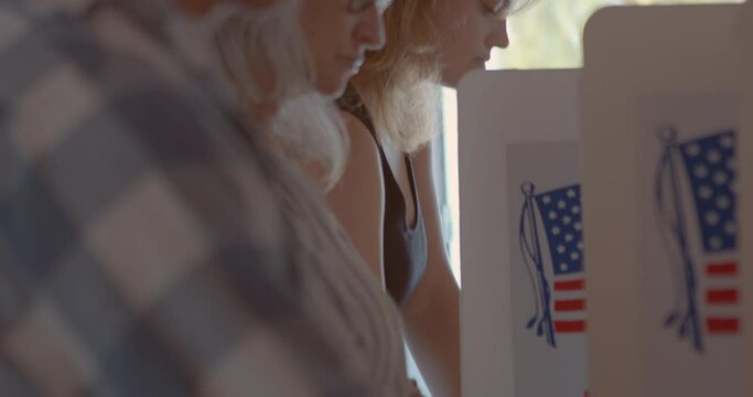 Close up on a diverse group of voters at a polling station concentrating and voting on their political choices with American Flag in the background