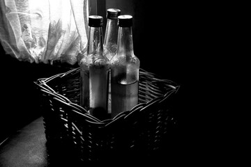Several bottles are in a rattan basket isolated on a dark background, empty drink bottles in the...