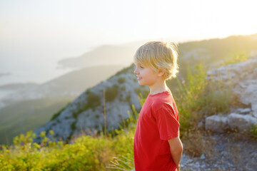 Cute boy admiring of Budva Riviera view from Fort Kosmach at sunset. Old fortress ruins is located in mountains near Budva in Montenegro. Panoramic landscape of Adriatic coast
