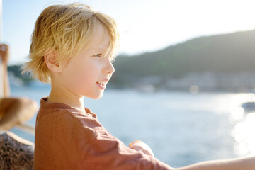 Cute blonde preteen boy is traveling by boat or ferry on the sea. Family vacations on ocean or sea. Summer leisure for families with kids.