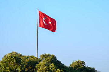 Waving flag of the Republic of Turkey against the blue sky. It is a red rectangular panel with a...
