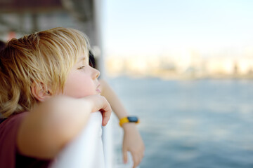 Cute blonde preteen boy is traveling by boat or ferry on the sea. Family vacations on ocean or sea. Summer leisure for families with kids. Child overheated on a hot sunny day.
