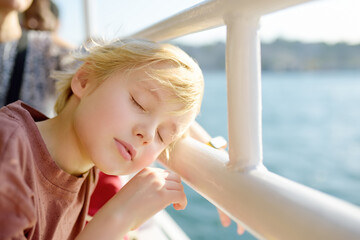 Cute blonde preteen boy is traveling by boat or ferry on the sea. Family vacations on ocean or sea. Summer leisure for families with kids. Child overheated on a hot sunny day.