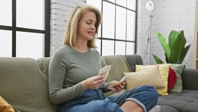 Young woman counts czech koruna bills on a sofa indoors, portraying a cozy finance concept at home.