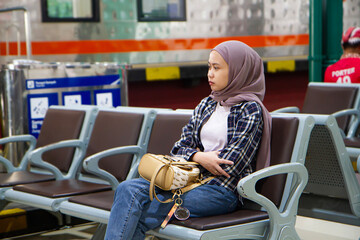 pensive asian woman sitting on the bench in the train station waiting room. traveling concept