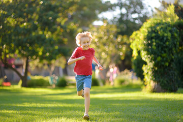 Elementary school child running on lawn in urban park on sunny day. Happy preteen boy having fun during walk. Outdoors activity for kids on summer holidays