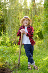 Little schoolboy holding with shovel on the domestic garden at summer sunny day. Family gardening activity with elementary school children.