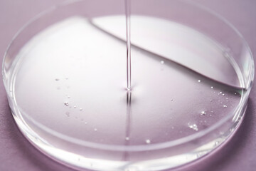 Serum or cosmetic oil flows into a transparent bowl on a purple background.