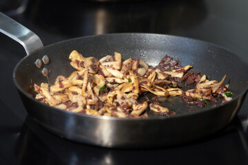 Cooked sliced mushrooms in a pan on electronic stove in kitchen.