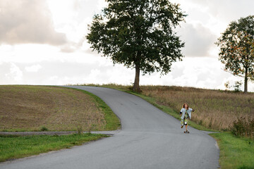 Quiet countryside. Beautiful girl glides on longboard from afar.