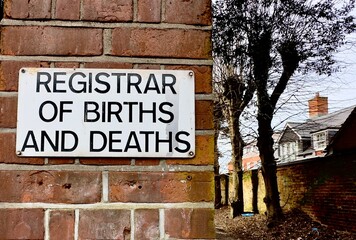 A closeup of a sign for the Registrar of Births and Deaths on a brick wall in the UK. 