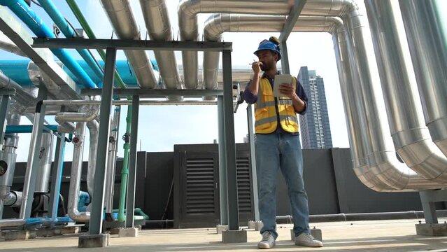 Foreman engineer wearing reflective jacket, engineering helmet, talking walkie talkie and holding tablet inspecting plumbing system, safety and maintenance on rooftop of construction building.