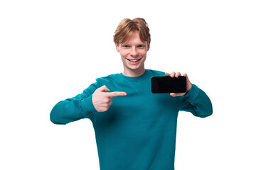 young handsome red-haired man with a blue sweater points a finger at a smartphone