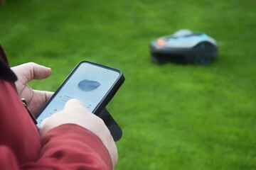 A man controls a robotic lawnmower using a phone app.