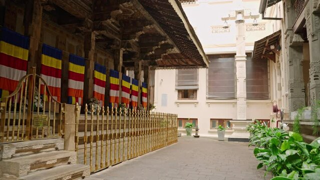 Interior of Sri Dalada Maligawa, Kandy, with vibrant Buddhist flags, gold railings guard sacred space. Pilgrims visit temple, cultural heritage site in serene compound, Buddhism ritual practice area.