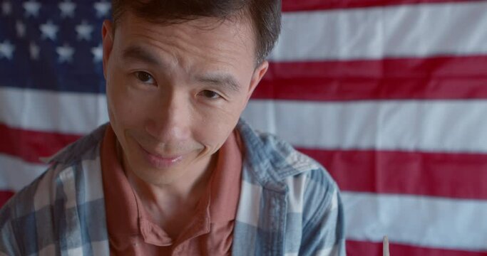 Close up of an Asian man in a voting booth at a polling station with an American flag in the background