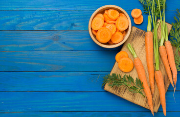 Bunch of fresh carrots with sliced ones on wooden background, top view