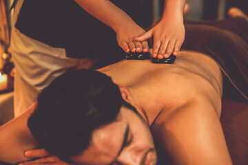 Hot stone massage at spa salon in luxury resort with warm candle light, blissful man customer...