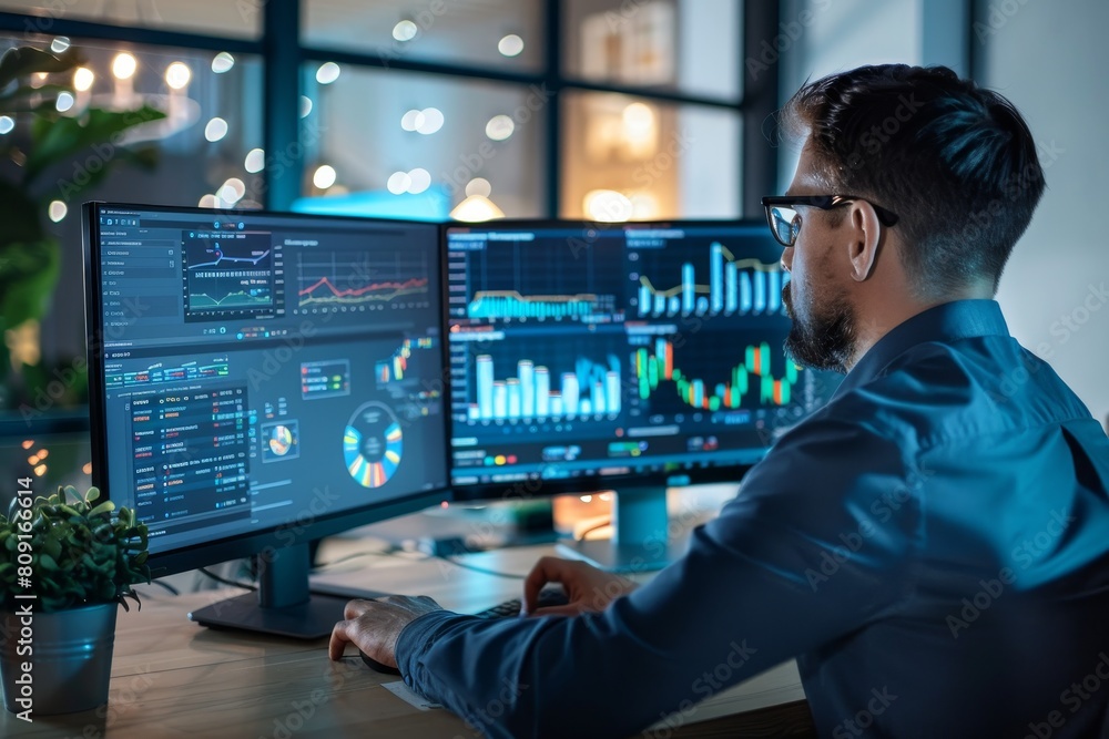 Poster a man is seated at a desk, focusing on charts and graphs displayed on two computer monitors, a busin