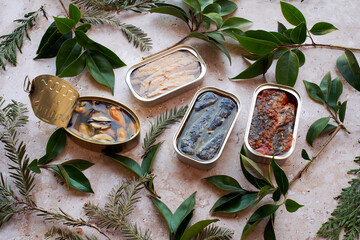 Several cans of seafood surrounded by fresh green leaves.